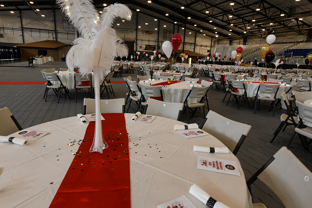 table setup for party in indoor arena, white tablecloth, red runner, feather and balloon centerpiece